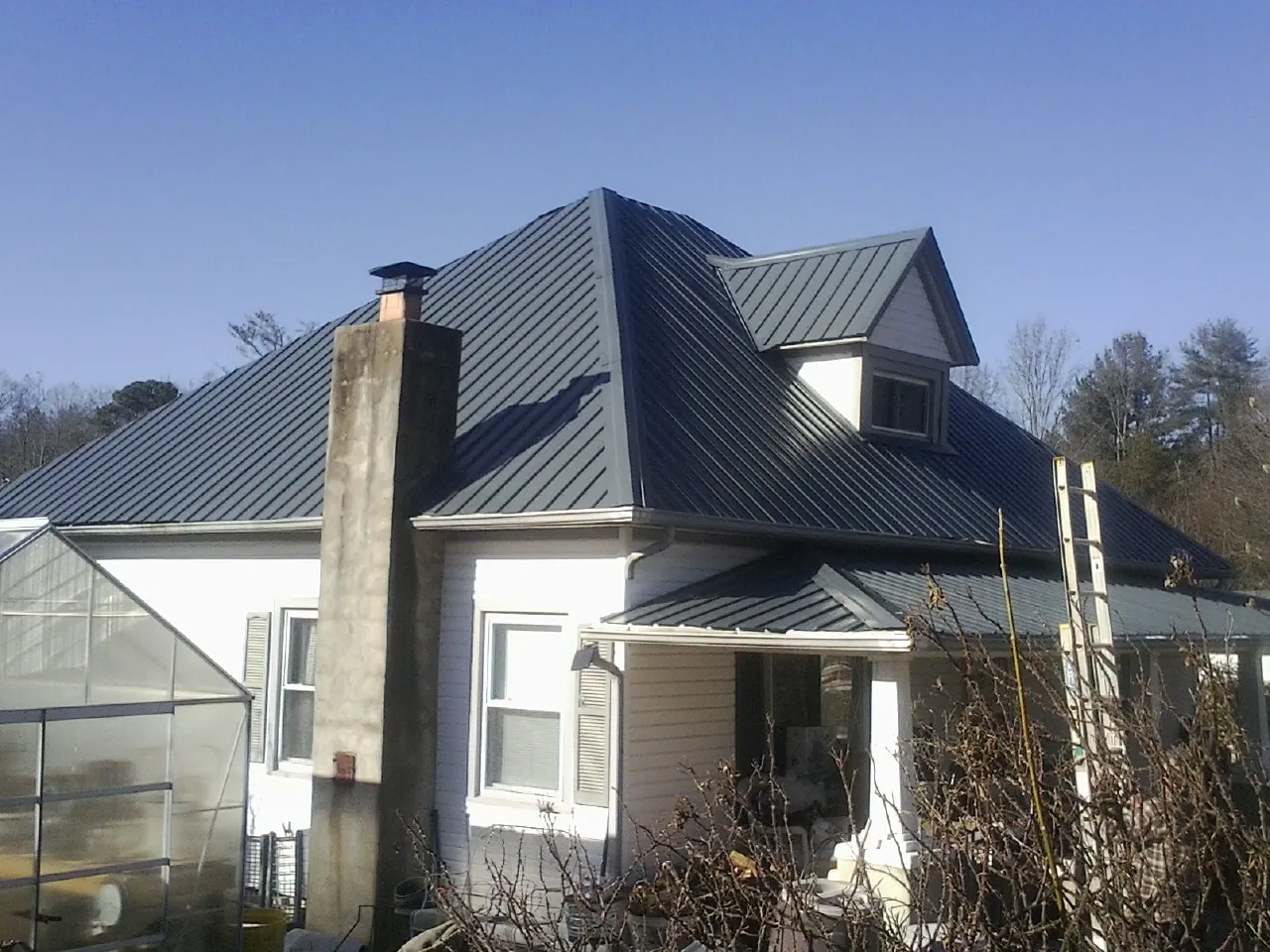 Dark blue standing seam metal roof on a white farmhouse with dormer — Slate & Tile Roof Repair by Roofing Brothers in Honey Grove