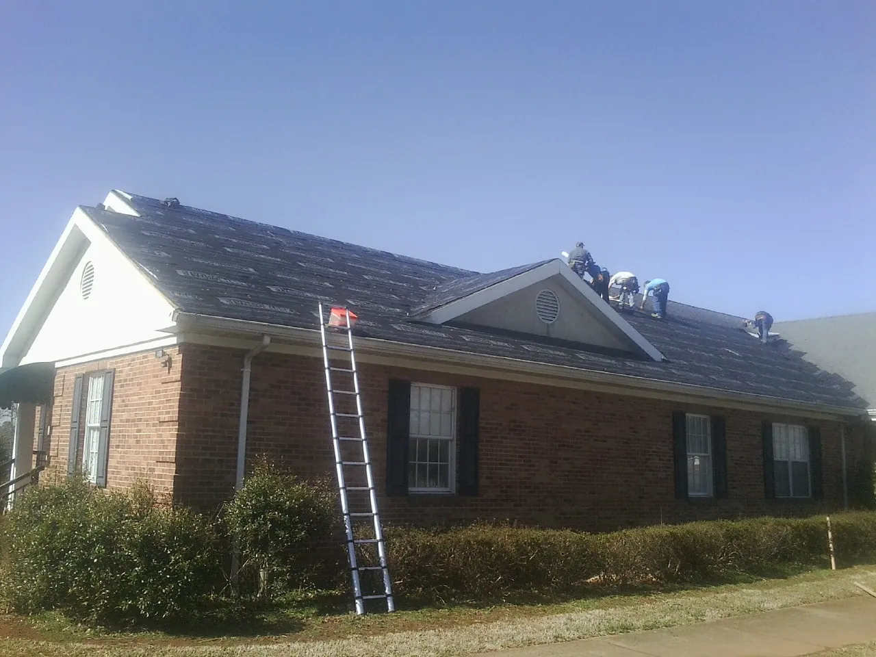 Crew tearing shingles off a brick ranch roof with a ladder set — Emergency Roof Repair work by our crew in Honey Grove