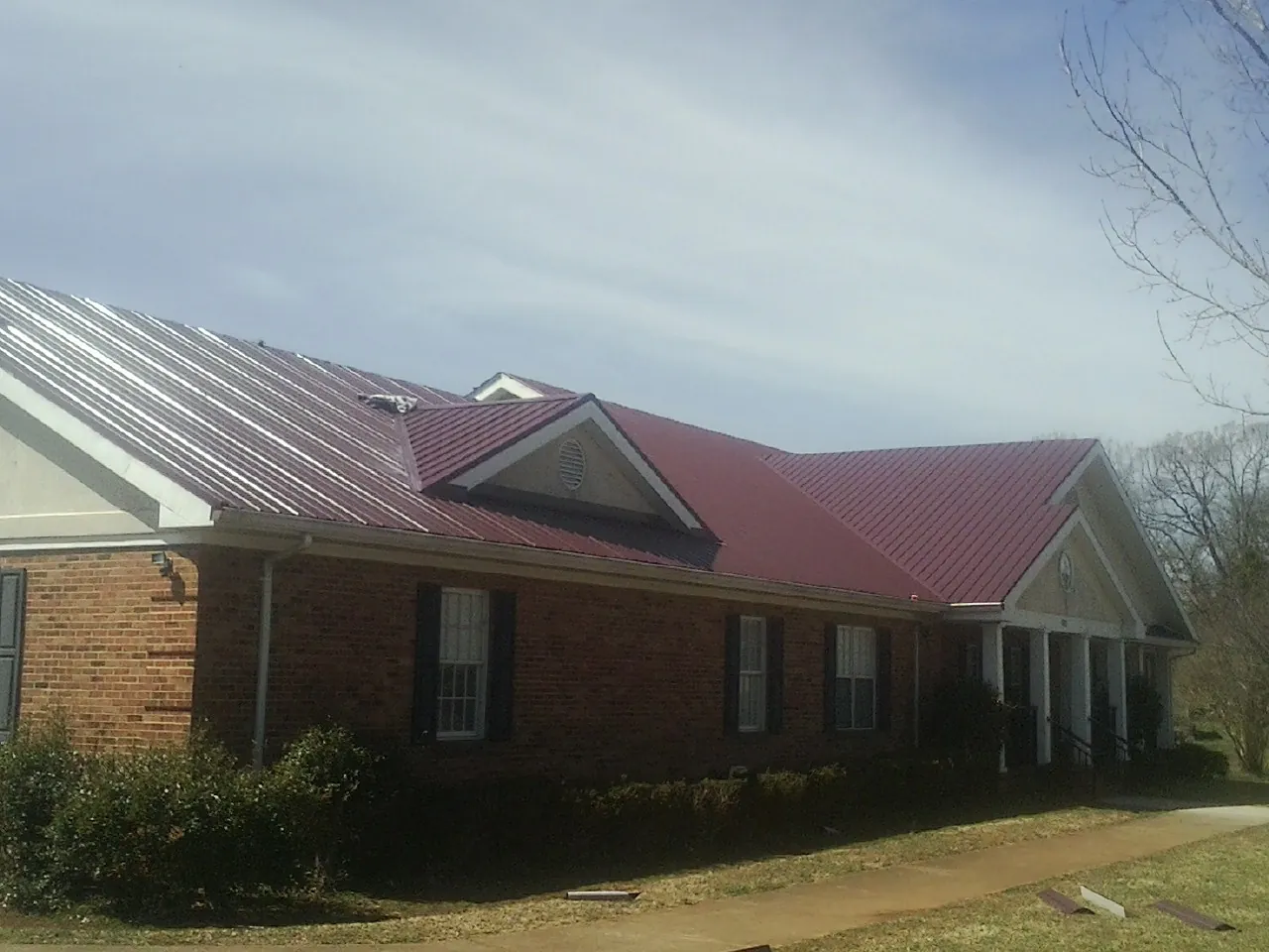 Red metal roof with gabled entries on a long brick building, from a Hail Damage Roof Repair job in Honey Grove