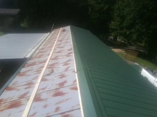Old rusted panels beside newly installed green metal roofing — Wind Damage Roof Repair by Roofing Brothers in Honey Grove
