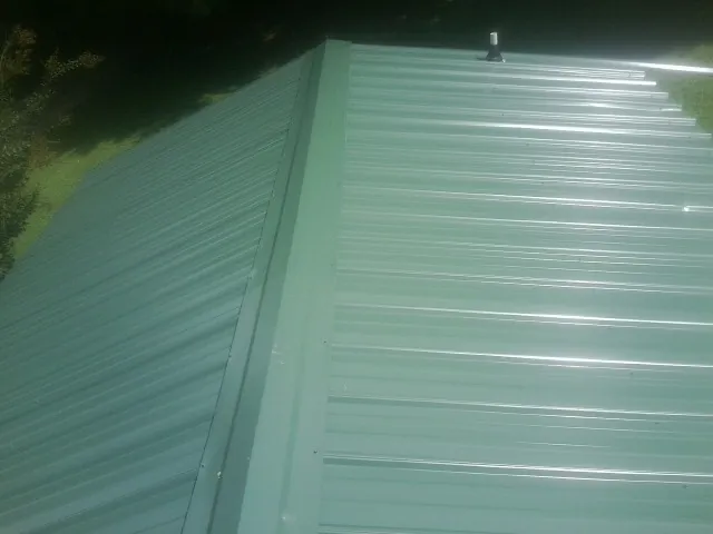 New green metal panels meeting at the ridge of a roof — Flat Roof Repair work by our crew in Honey Grove