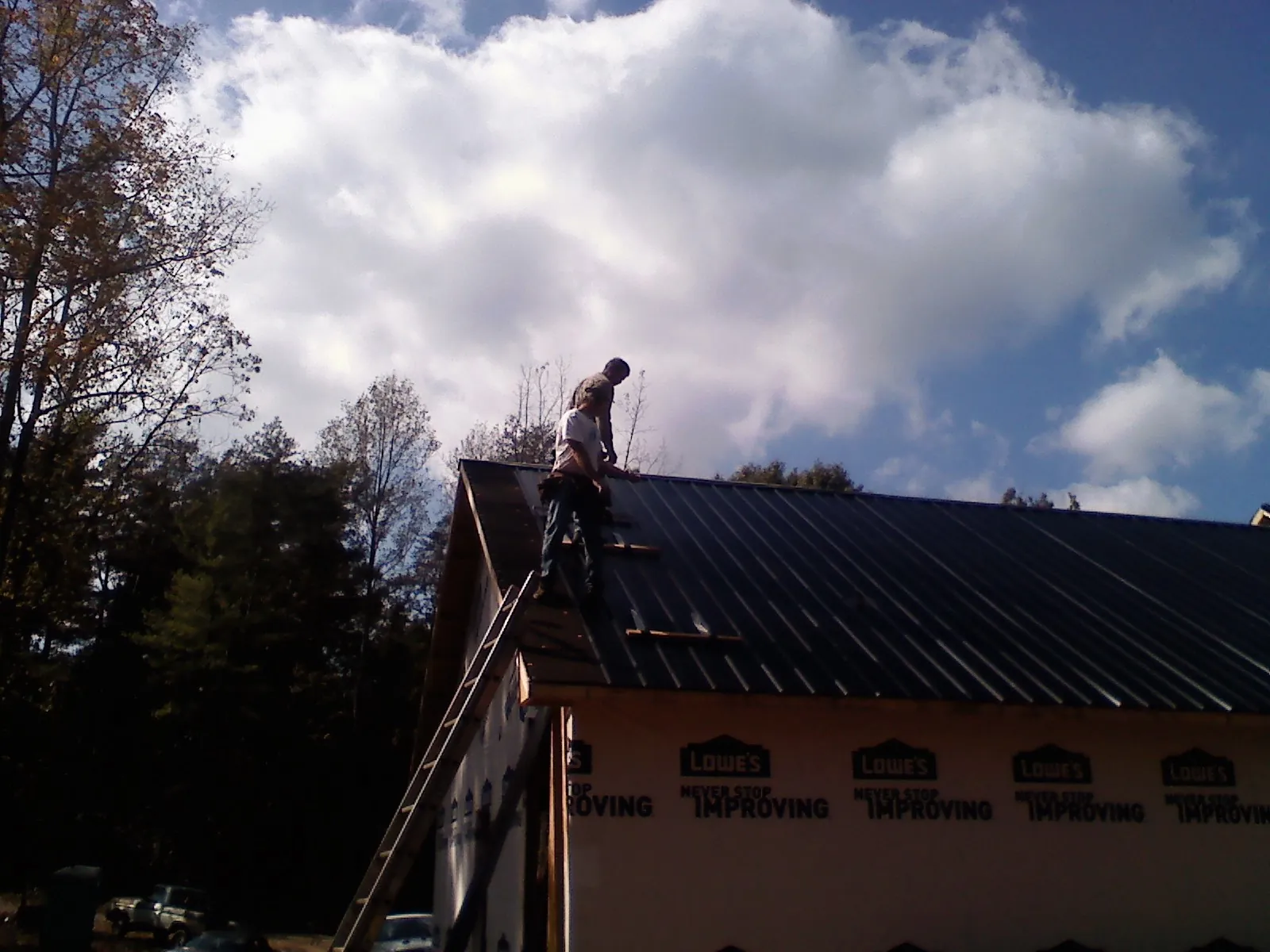 Roofer fastening dark metal panels high against a cloudy sky, from a Roof Inspection job in Honey Grove