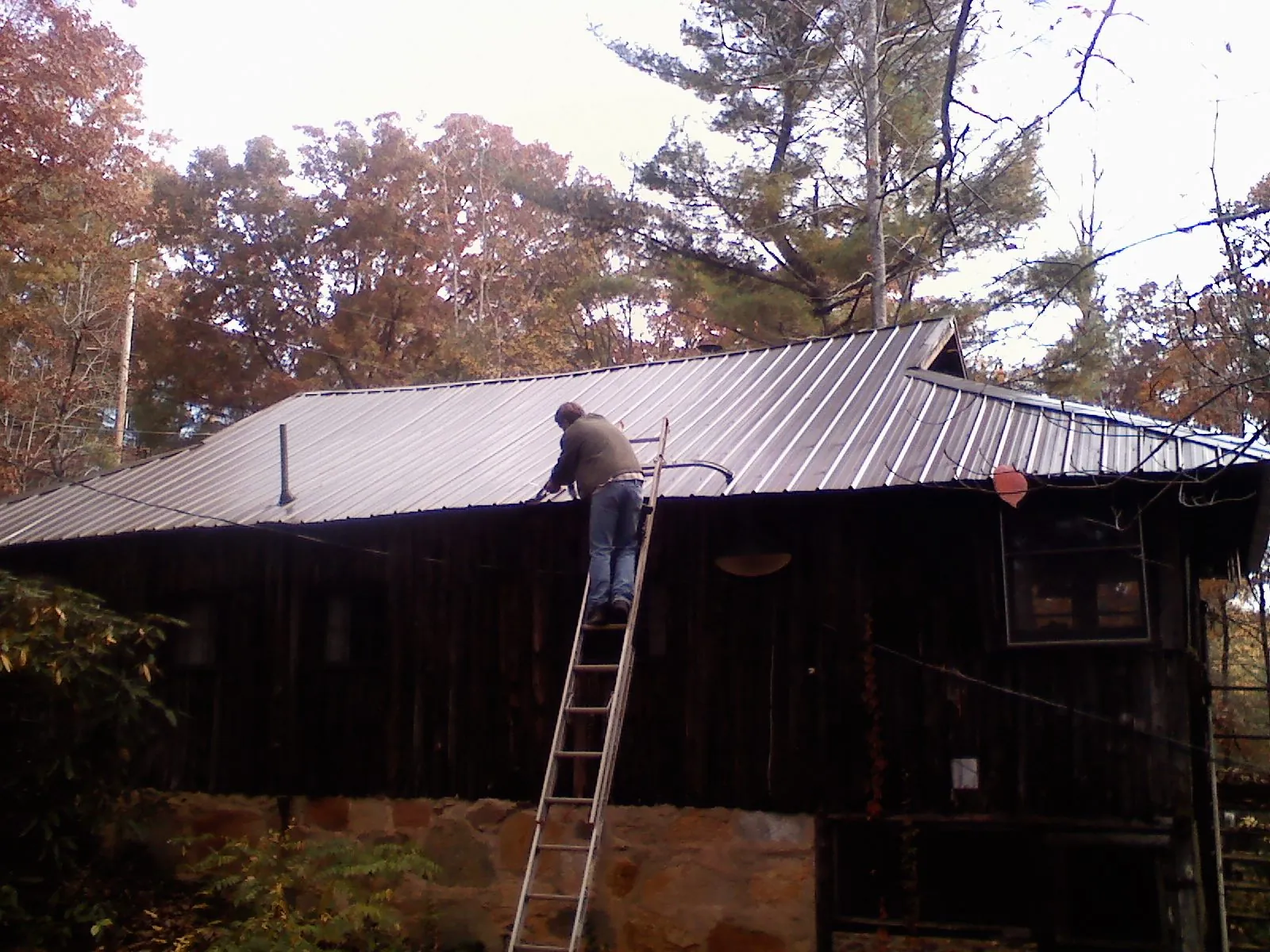 Roofer on a ladder working along the edge of a cabin metal roof in Honey Grove