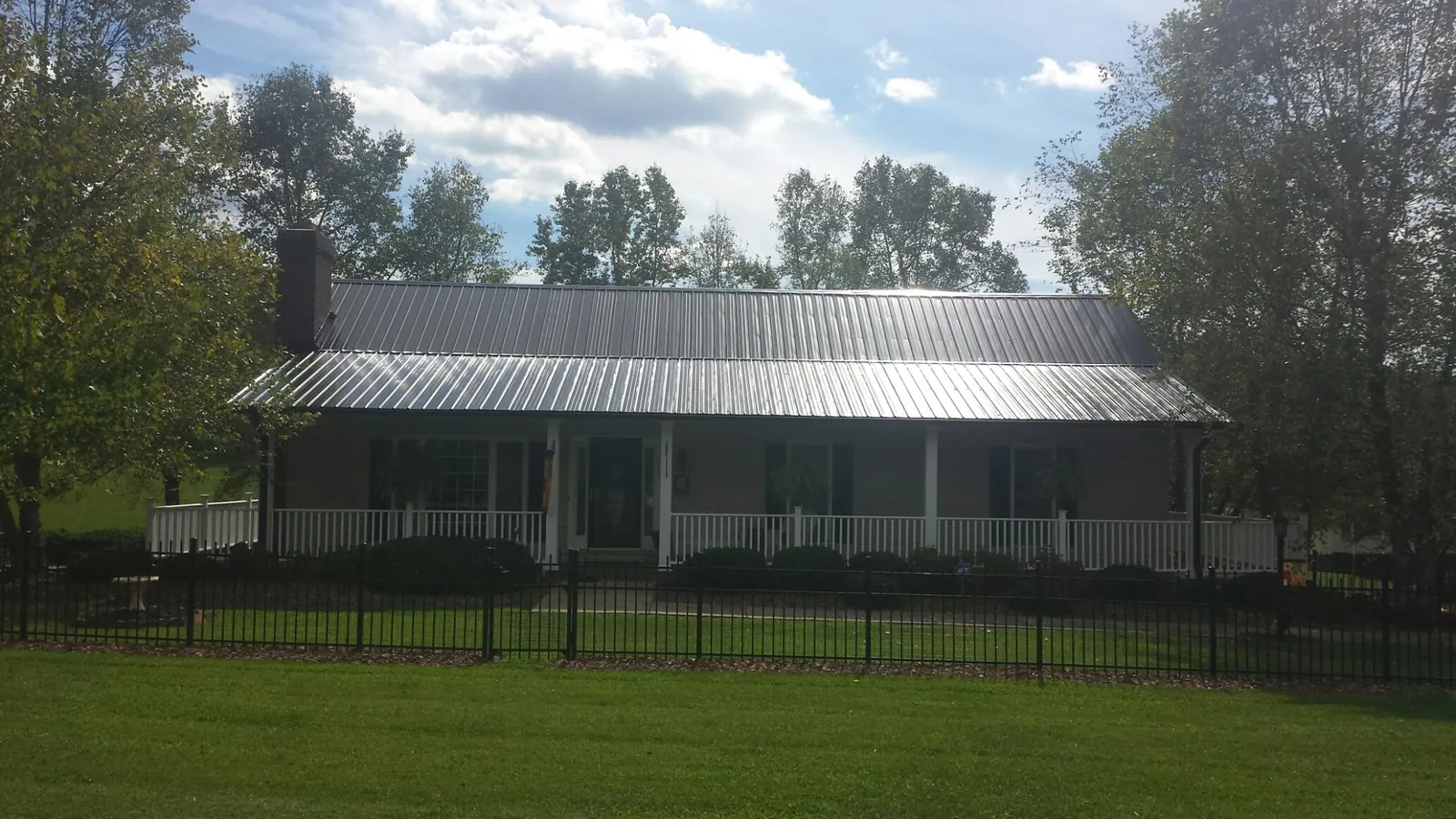 Gray metal roof on a brick ranch with a full width front porch — Gutter Guard Installation work by our crew in Honey Grove