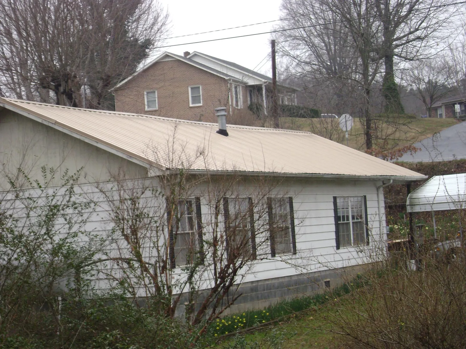 Tan metal roof on a white sided house set into a hillside — Commercial Roofing by Roofing Brothers in Honey Grove