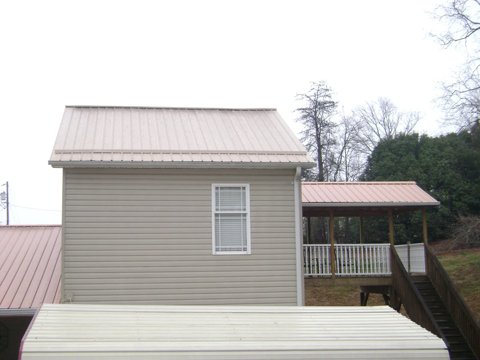 Tan metal roofs on a two story addition and attached porch, from a Roof Replacement job in Honey Grove